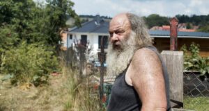 Foto. Älterer Herr mit langem Bart im Seitenprofil vor einem Gartenzaun