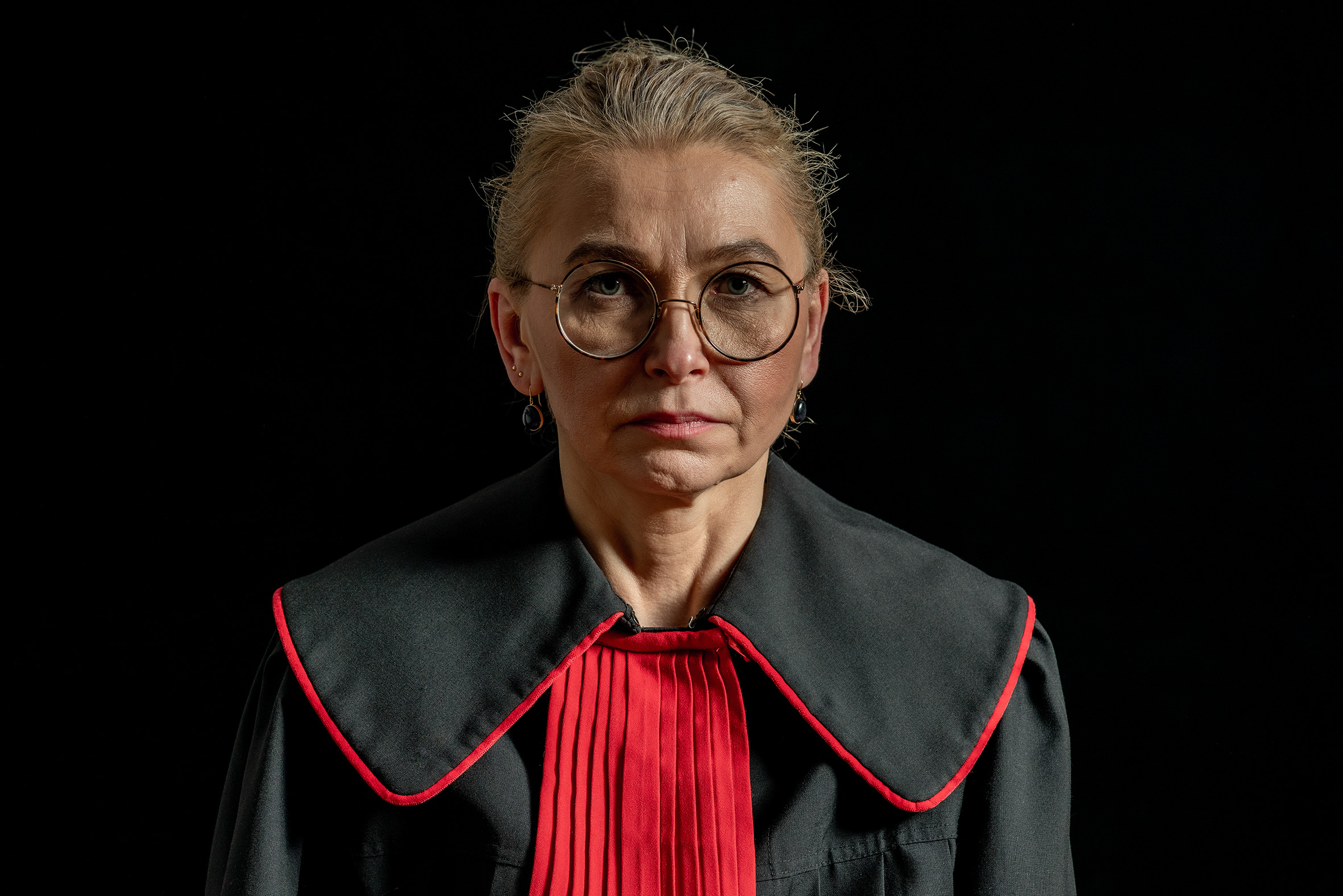 das Porträt einer widerständigen polnischen Richterin, die eine schwarz-rote Robe trägt und streng in die Kamera blickt
