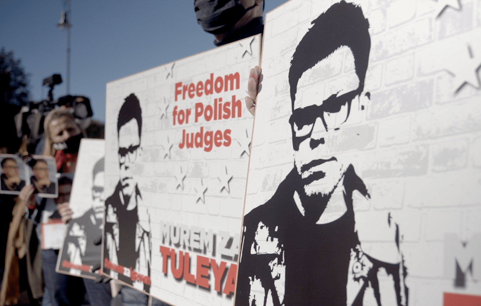 Ein Banner auf einer Mauer in Polen mit dem Gesicht des Richters Igor Tuleya; im Hintergrund Demonstrant:innen