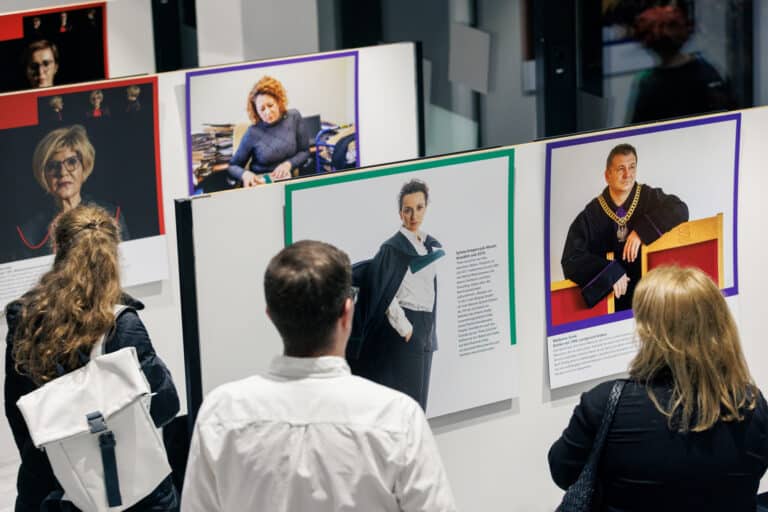 Drei Menschen schauen sich die Fotos der Ausstellung Sprawiedliwość - Gerechtigkeit an