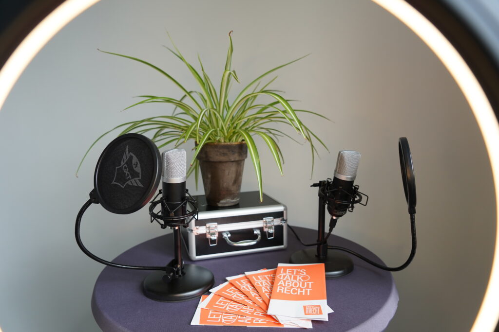 Podcast-Situation: zwei Mirkophone auf einem Tisch, daneben Flyer der Stiftung Forum Recht und eine Zimmerlilie.