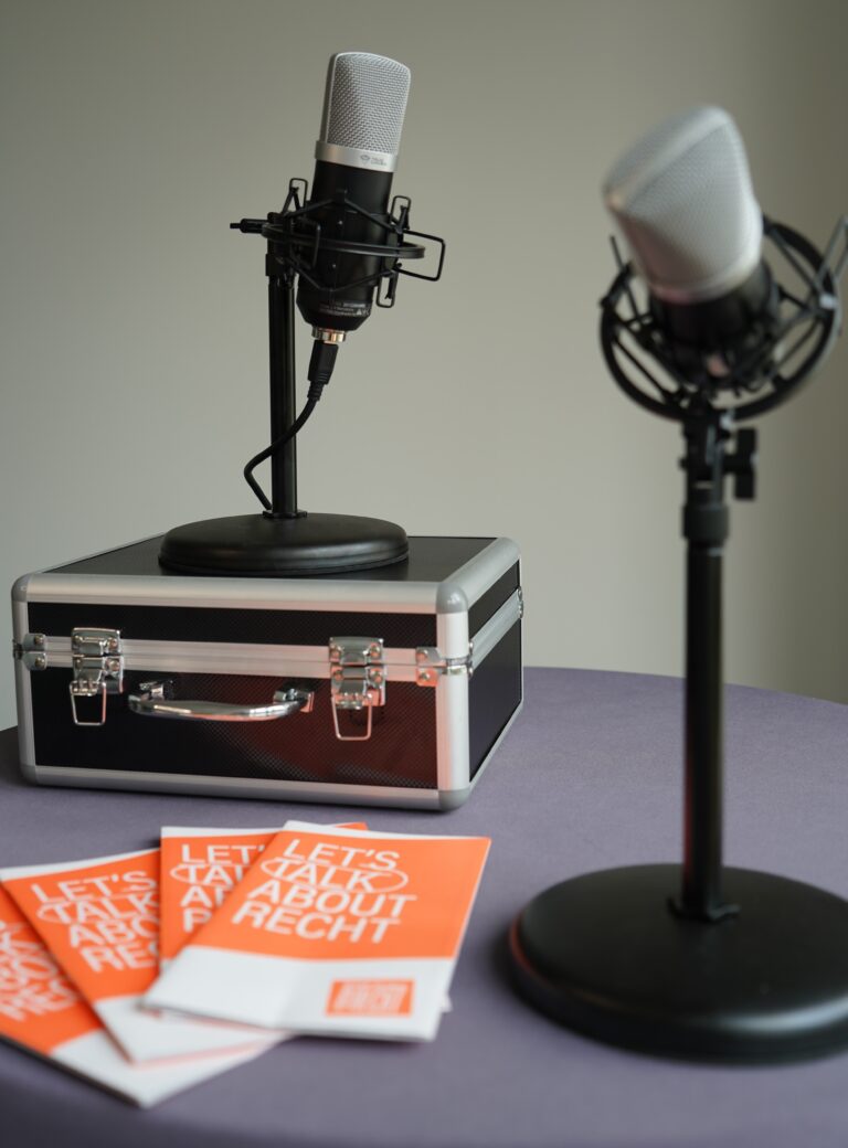 Podcast-Situation: zwei Mirkophone auf einem Tisch, daneben Flyer der Stiftung Forum Recht.