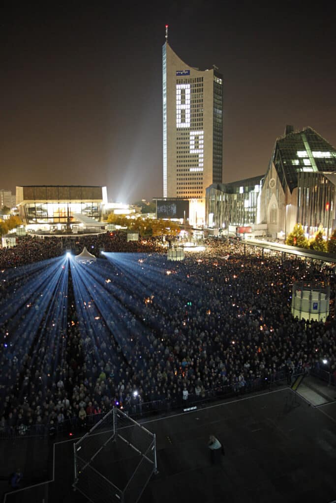 Mernschenmassen in der Leipziger Innenstadt erstrahlt von Licht-Installation. Im Hintergrund das Schauapielhaus und der MDR-Turm.