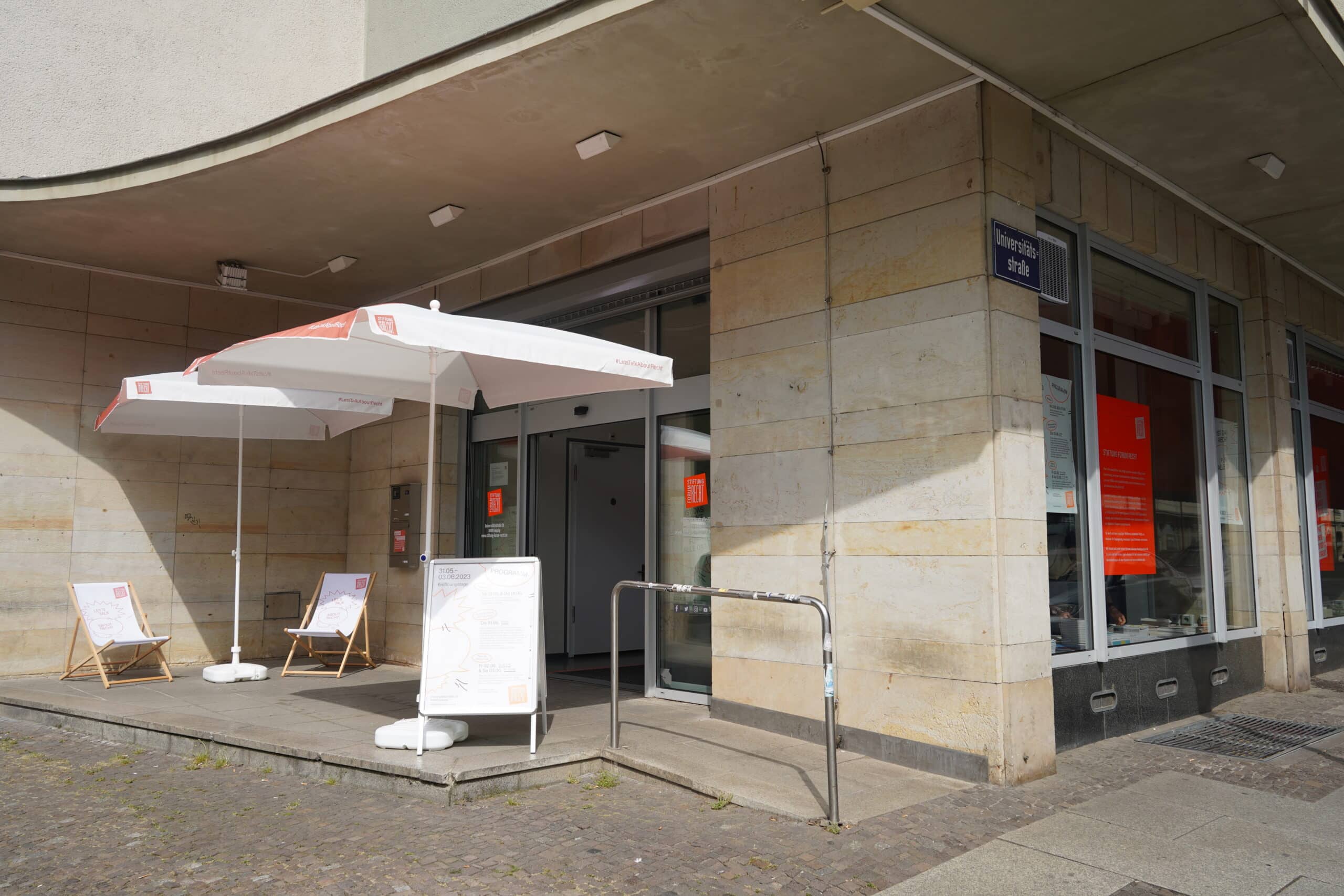 Eingangsbereich der Stiftung Forum Recht in Leipzig mit Sonnenschirmen und Liegestühlen.