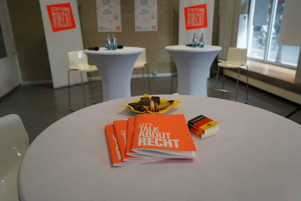 Zwei Mini-Grundgesetze, Kekse und vier Notizblöcke der Stiftung Forum Recht liegen auf einem Stehtisch, der im Raum steht.