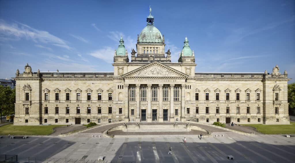 Frontansicht Bundesverwaltungsgericht Leipzig. Ein sehr großes, barockes Gebäude mit grünlichem Kuperfdach bei Sonnenschein.