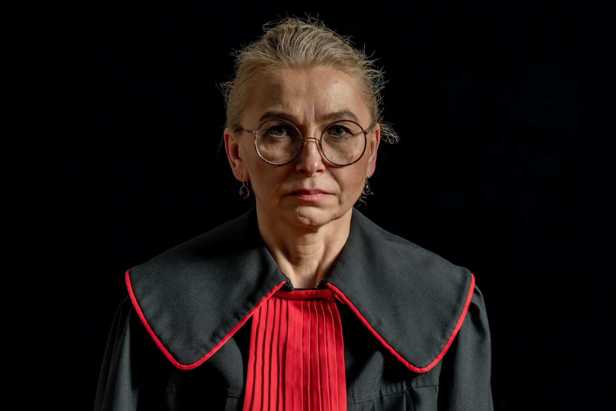 Das Porträt einer widerständigen polnischen Richterin, die eine schwarz-rote Robe trägt und streng in die Kamera blickt