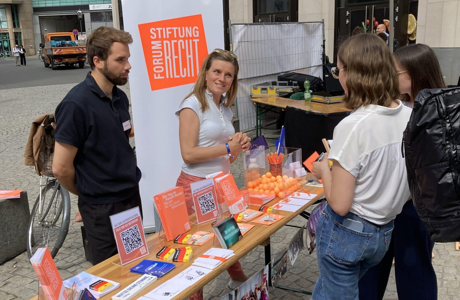 Zwei Mitarbeiter der Stiftung stehen im Sommer hinter einem Infostand der Stiftung auf dem Burgplatz in Leipzig