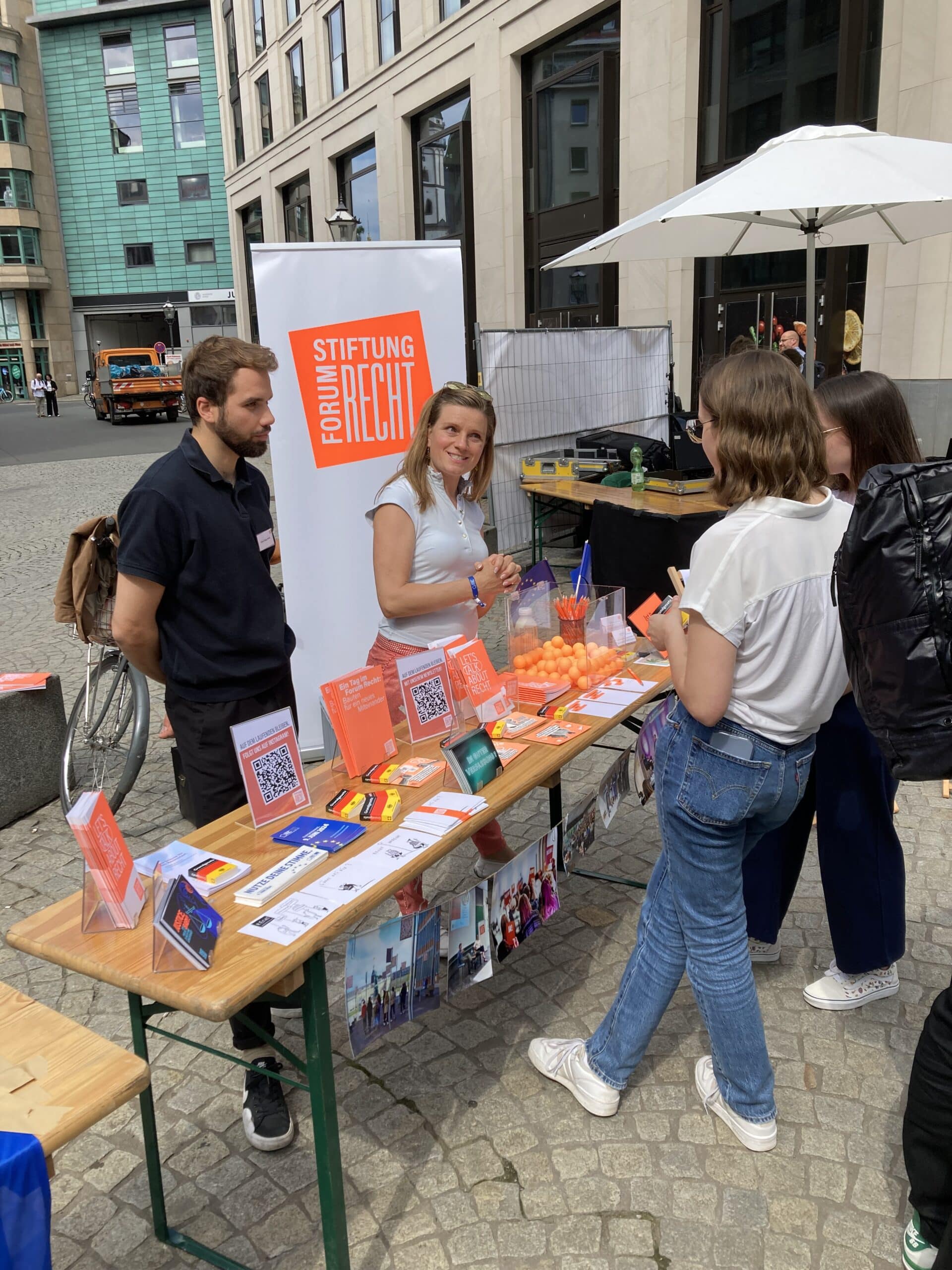 Zwei Mitarbeiter der Stiftung stehen im Sommer hinter einem Infostand der Stiftung auf dem Burgplatz in Leipzig