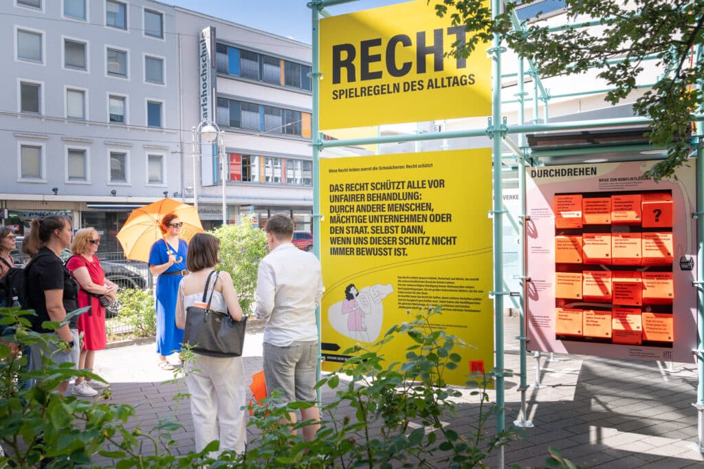 Ausstellung vor der Stiftung Forum recht weird am Tage von Menschen mit orangen Stiftungs-Sonnenschirmen besucht.