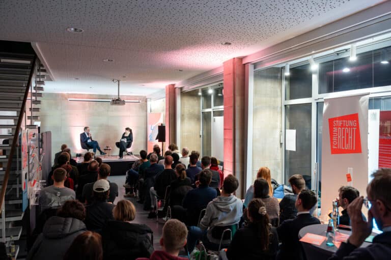 Publikum in den Leipziger Räumen der Stiftung mit Blick zur Bühne, auf der ein Mann und eine Frau ins Gespräch vertieft sind.