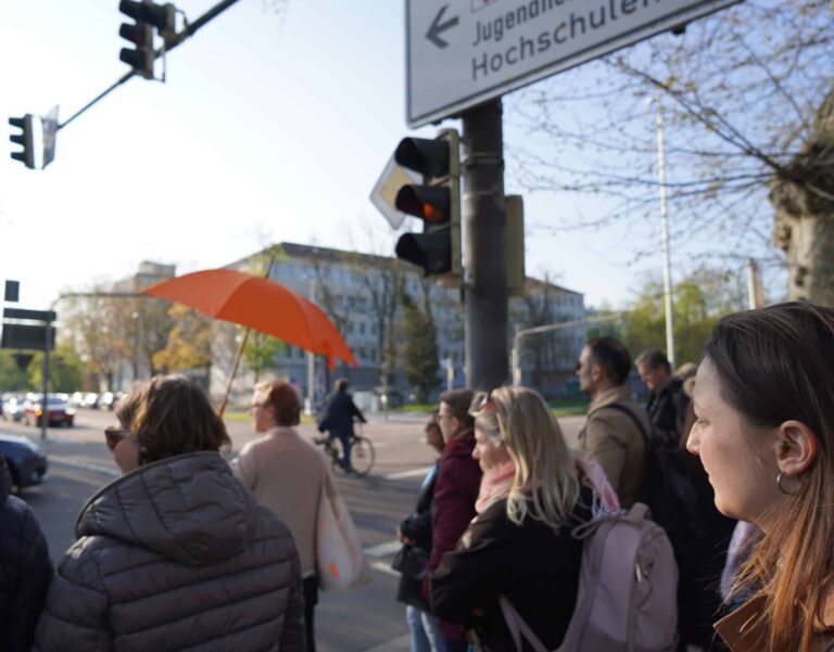 Eine Gruppe an der Ampel folgt einem Mann mit orangem Schirm.
