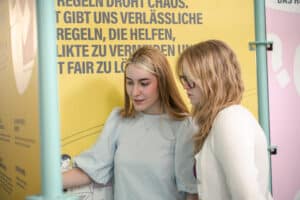 Zwei Personen stehen vor einer Wand der Pop-Up-Ausstellung und interagieren mit dem Inhalt
