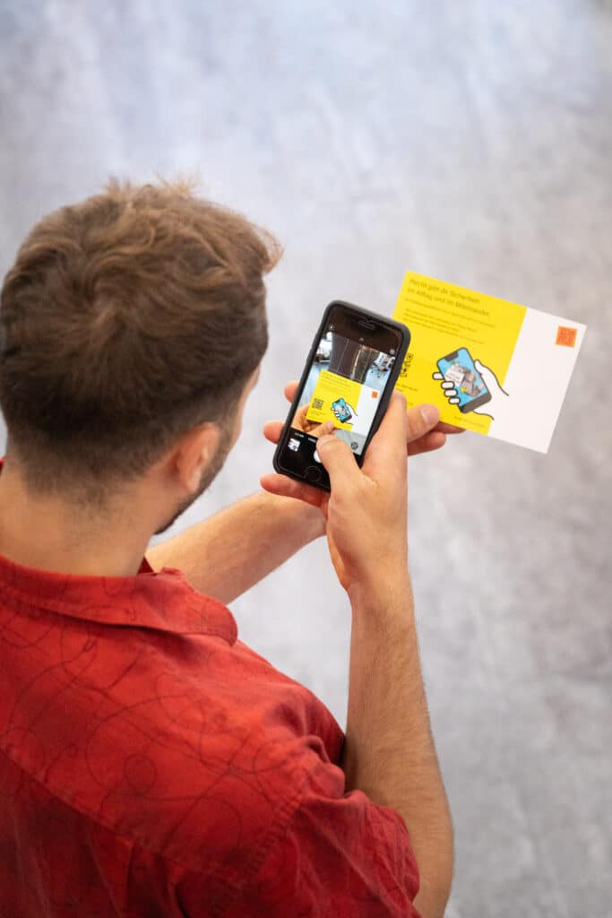 Junger Mann mit rotem Hemd wird von hinten und oben dabei fotografiert, wie er das Beteiligungstool auf dem Smartphone bedient