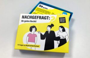 Eine offene Pappschachtel in gelb, darauf steht: "Nachgefragt: Ihr gutes Recht! 75 Fragen zu Recht & Rechtsstaat"
