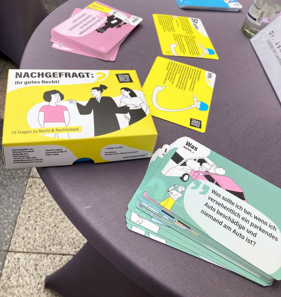 Auf einem Stehtisch liegen mehrere Postkarten mit Fragen und Illustrationen. Daneben eine Pappschachtel mit der Aufschrift "Nachgefragt: Ihr gutes Recht!"