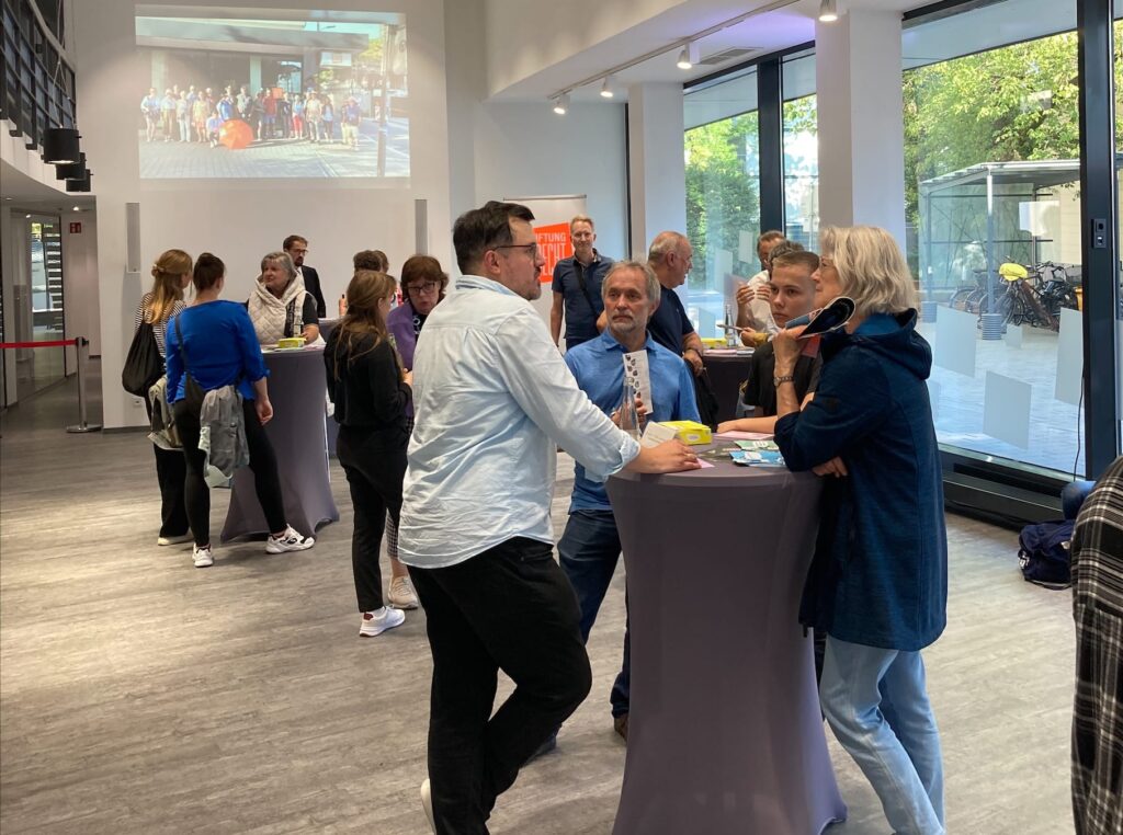 Eine Gruppe Besucher steht an Stehtischen in den Räumen der Stiftung Forum Recht