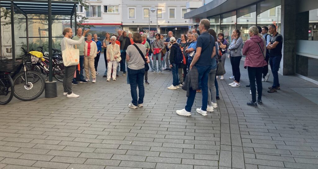 Eine Gruppe Menschen steht bei Sonnenlicht auf dem Parkplatz vor den Räumen der Stiftung Forum Recht