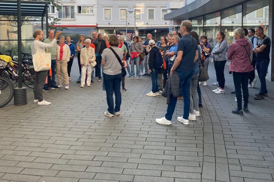 Eine Gruppe Menschen steht bei Sonnenlicht auf dem Parkplatz vor den Räumen der Stiftung Forum Recht