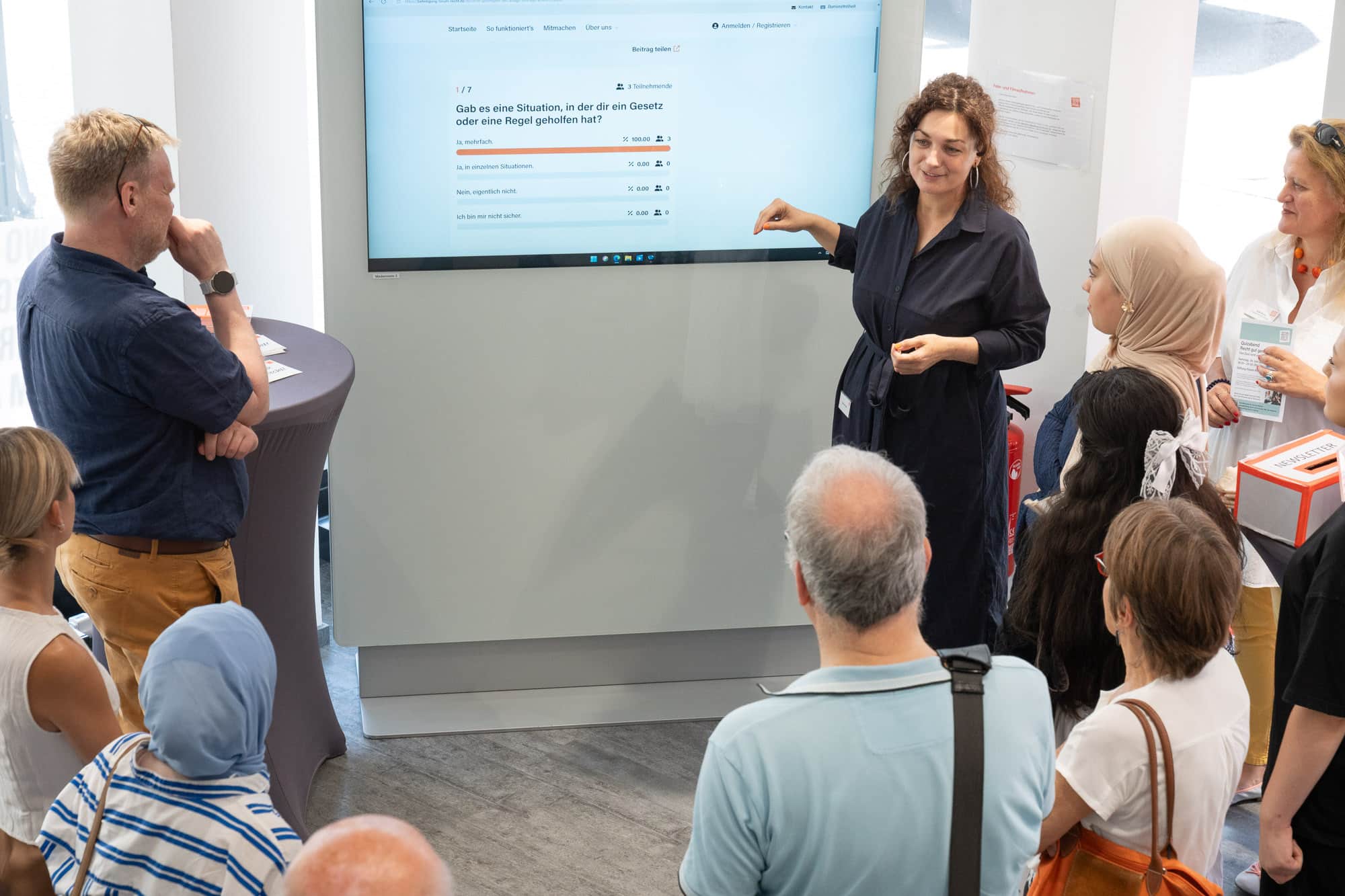 Eine Frau erklärt an einem großen Bildschirm einem Publikum eine digitale Umfrage.