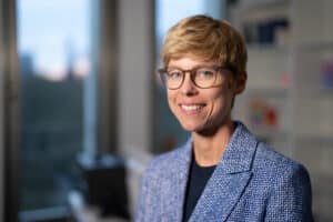 Eine junge Frau mit blonder Kurzhaarfrisur und einer Brille lächelt in die Kamera.