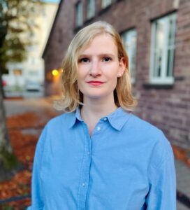 Porträt einer jungen Frau mit blondem halblangem Haar und rotem Lippenstift.