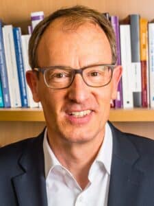 Porträt eines mittelalten, lächelnden Mannes mit Brille.