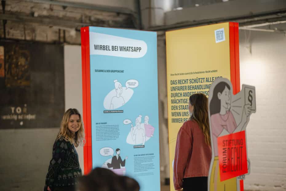 Leuchtstehlen der Indoor-Ausstellung "Recht - Spielregeln des Alltags" mit Menschen davor, die sie betrachten.