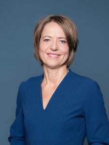 Lächelnde Frau mit blondem haar in einem marineblauen Kostüm.