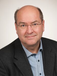Älterer Mann mit Brille, in Hemd und Sakko.