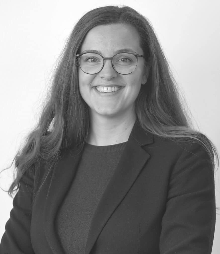 Junge Frau mit Brille und langen Haaren lächelt in die Kamera.