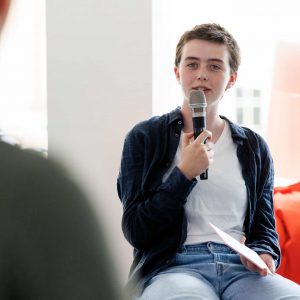 Eine junge Frau hält ein Mikrofon in der Hand und spricht in einer Interviewsituation.