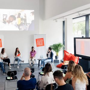 Veranstaltung mit Besucherinnen und einer Gruppe junger Rednerinnen im Bildhintergrund.