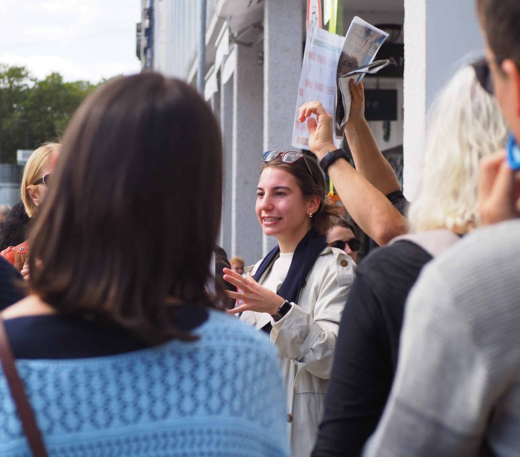 Eine junge Mitarbeiterin der Stiftung leitet die Teilnehmer:innen des Stadtrundgangs in Karlsruhe durch den Tag.